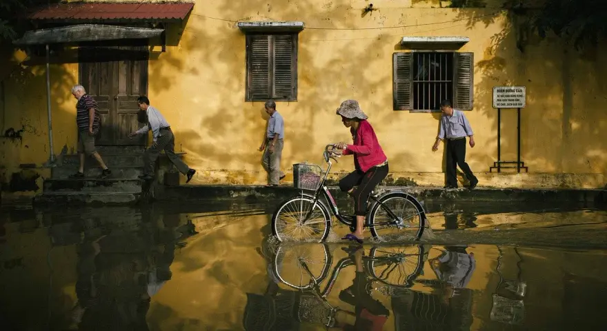 Une femme à vélo traverse une rue inondée, reflétant la vie quotidienne. Quel objectif pour photo de rue capture cette scène ?