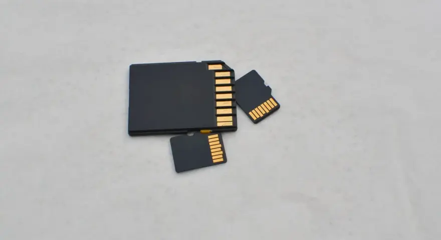 Trzy czarne karty pamięci: jedna większa, przypominająca kartę SD, oraz dwie mniejsze, typu microSD. Złote styki widoczne na każdej karcie.