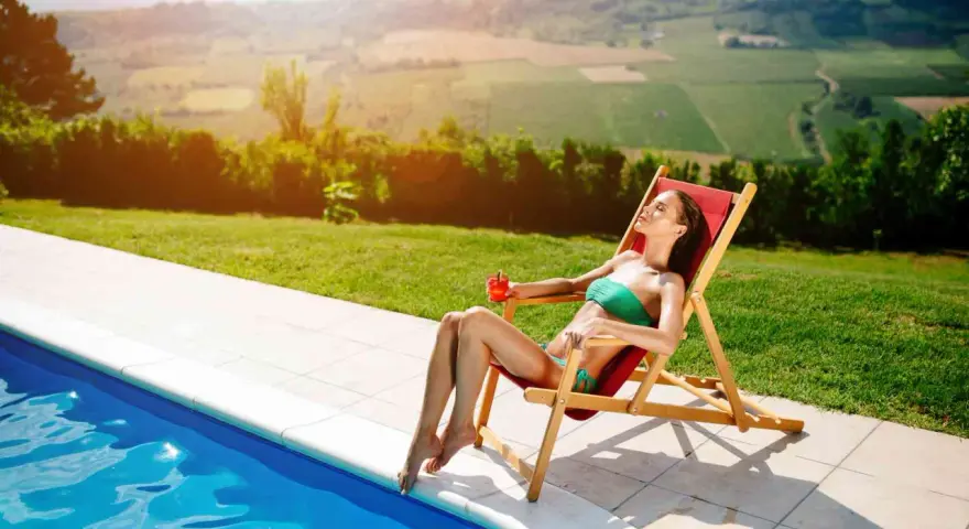 Donna rilassata su una sdraio, con drink, vicino a una piscina. Il sole splende, ideale per chi vuole sapere come abbronzarsi velocemente.