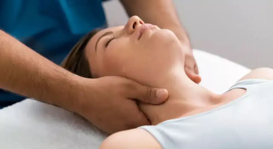 Fizjoterapeuta delikatnie masuje szyję kobiety, łagodząc napięcie. To jak ulga, gdy znika uczucie włosów w gardle.