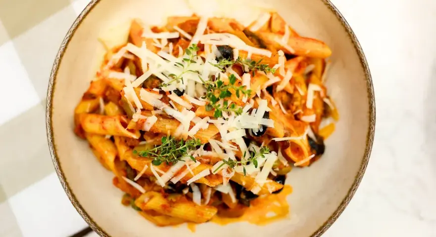 Penne z bogatym sosem anchois, czarnymi oliwkami i parmezanem, udekorowane świeżym tymiankiem.
