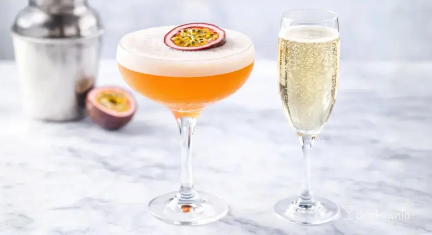 Pomarańczowy drink z pianką i marakują, obok kieliszek szampana. Idealny white lady drink na letnie popołudnie.