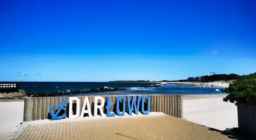 Napis "DARŁOWO" na tle plaży i morza. Darłówko zaprasza na wypoczynek nad Bałtykiem.