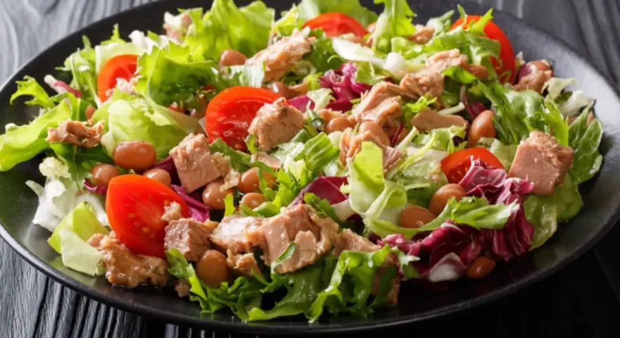 Ein frischer Thunfischsalat mit knackigem Salat, Tomaten und Bohnen auf einem schwarzen Teller.