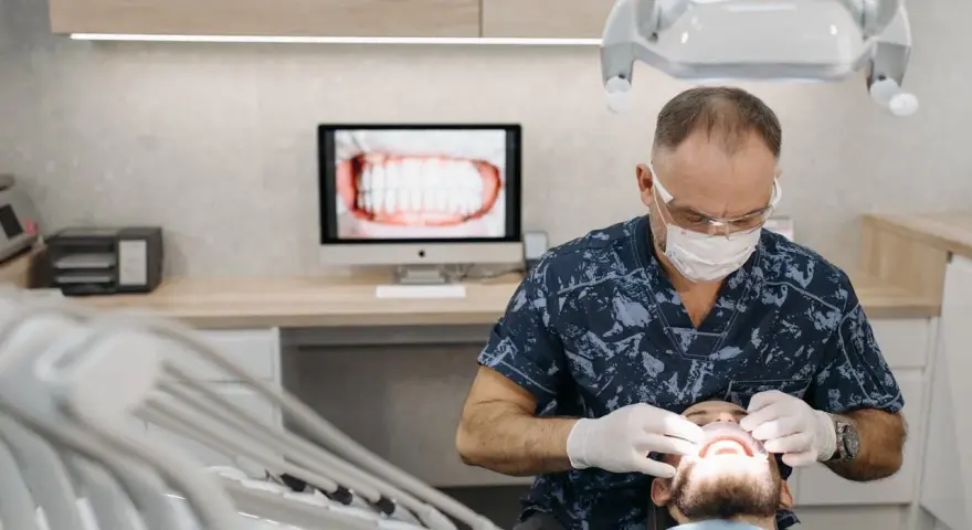 Dentysta w masce i rękawiczkach bada usta pacjenta.