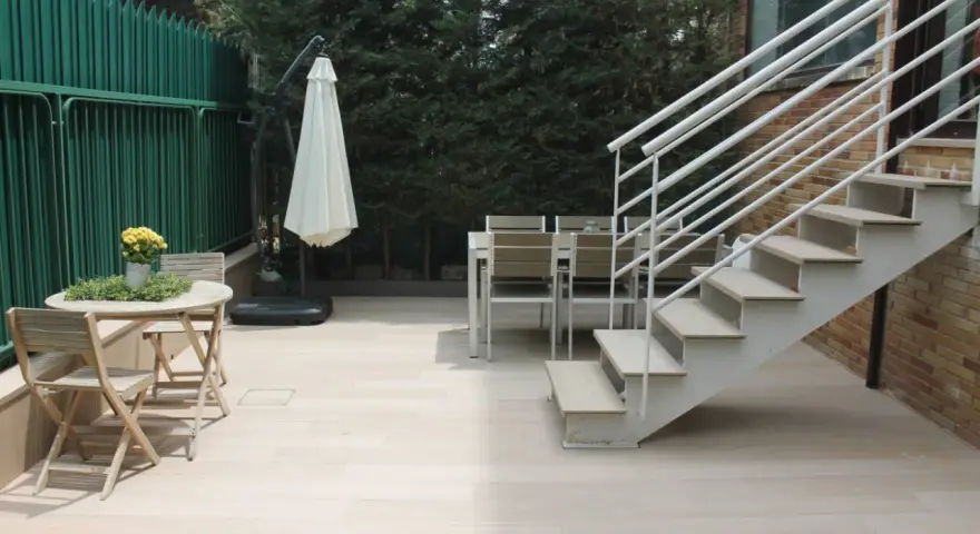 Escaleras exteriores casas de campo, con mesa y sillas de madera, sombrilla y valla verde.