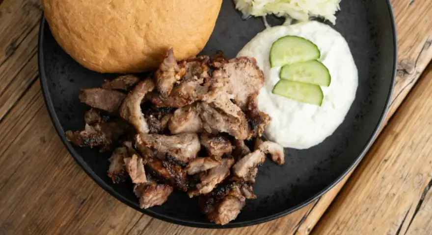 Ein Teller mit gegrilltem Fleisch, einem Brötchen, Tzatziki und Krautsalat. Perfekt für ein leckeres Gyros Rezept.