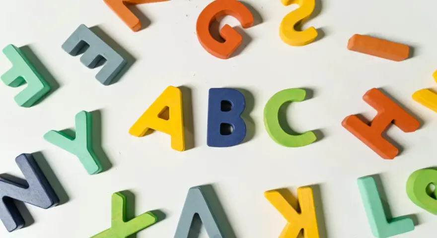 Kolorowe drewniane litery, idealne dla nauczyciela wychowania przedszkolnego, tworzą napis "ABC" i inne znaki.