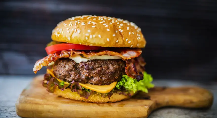 Soczysty burger z bekonem, serem i warzywami na desce.
