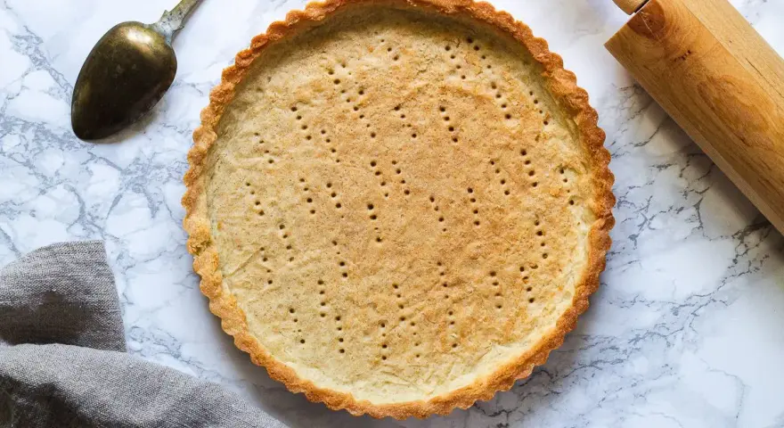 En gyllene pajskal, perfekt för ditt pajdeg recept. En kavel och en gammal sked ligger bredvid.