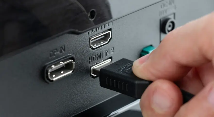 Hand steckt HDMI-Kabel ein, um den PC mit dem Fernseher zu verbinden. Anschlüsse für DisplayPort und HDMI sind sichtbar.