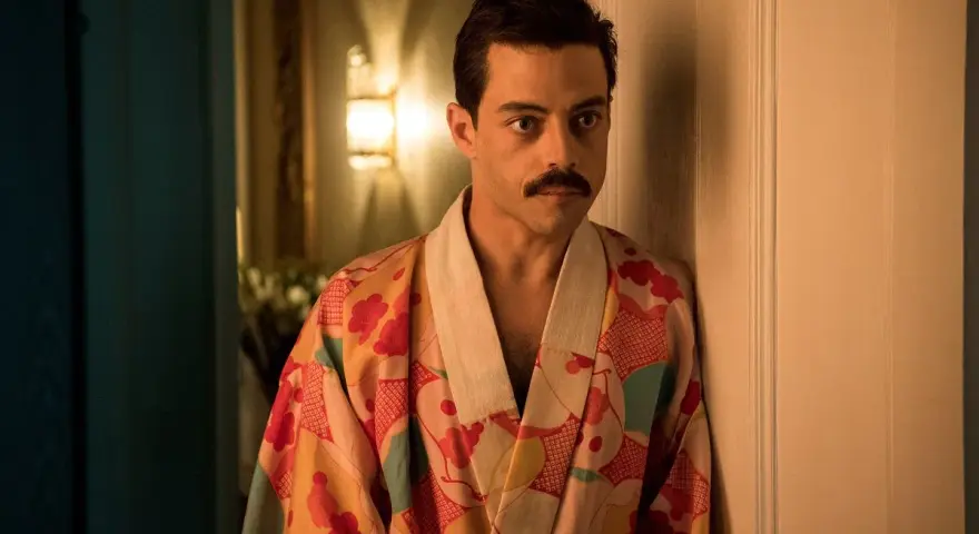 Freddie Mercury w barwnym szlafroku, jakby zrodzony z **bohemian rhapsody**, opiera się o drzwi.