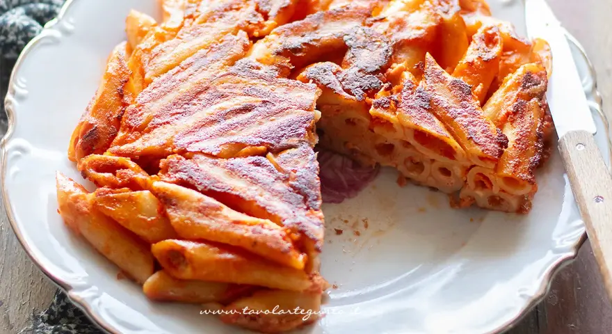 Una deliziosa frittata di pasta, dorata e croccante, servita su un piatto bianco con un coltello.