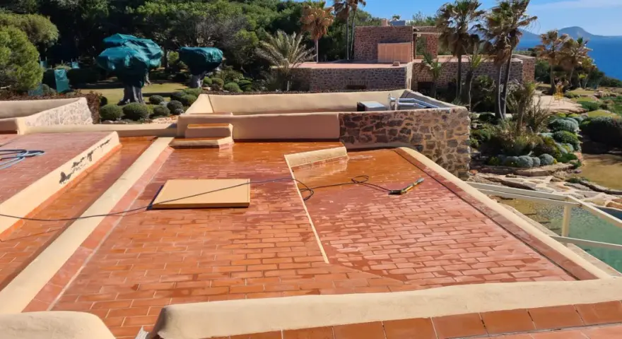 Proceso de impermeabilizar terraza con acabado de tejas rojas. El sol brilla sobre la superficie mojada, lista para proteger la casa.