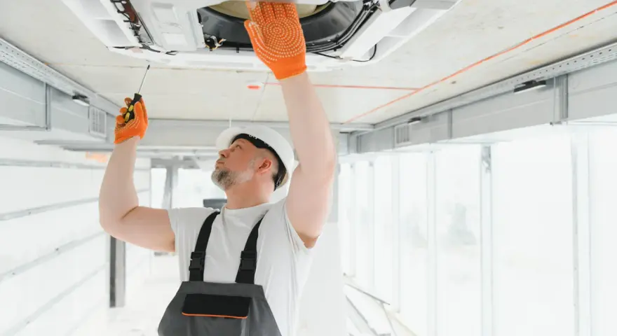 Técnico revisa aire acondicionado en techo, una señal para saber si le falta gas al aire acondicionado es que no enfría.