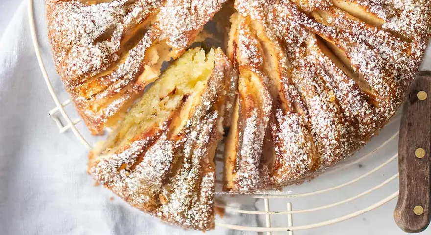 Deliziosa torta di mele in friggitrice ad aria, cosparsa di zucchero a velo, con una fetta tagliata che mostra la morbidezza dell'interno.