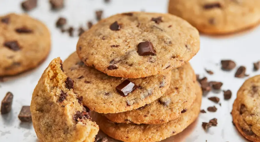 Ein Stapel saftiger american cookies mit Schokoladenstückchen, einer angeknabbert, umgeben von Schokoladenstückchen.