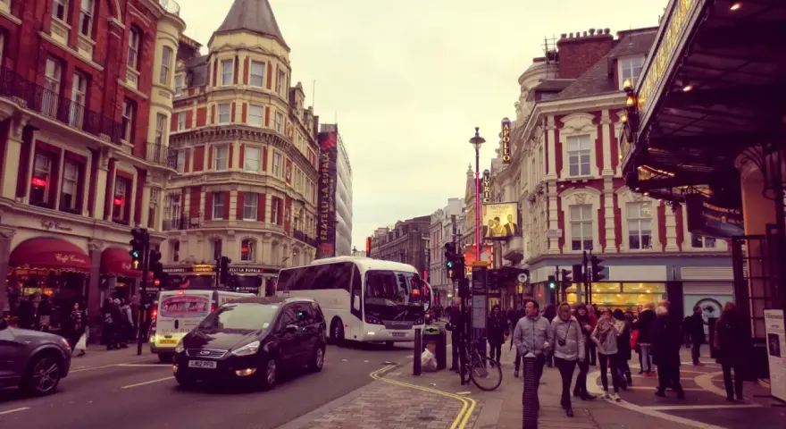 Tętniące życiem ulice Soho w Londynie, z charakterystyczną architekturą, autobusami i ludźmi spacerującymi po chodniku.