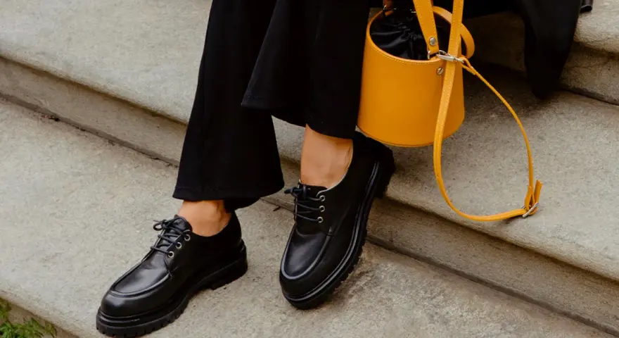 Come abbinare le stringate femminili: look audace con pantaloni neri e borsa gialla.