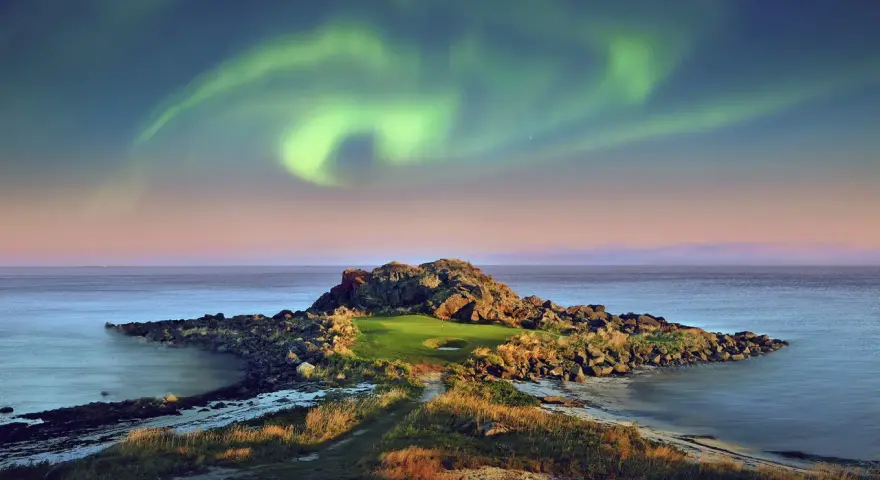 En unik golfbana i Norge under norrsken. En grönskande golfgreen omgiven av klippor och hav, med ett magiskt norrsken som lyser upp himlen.