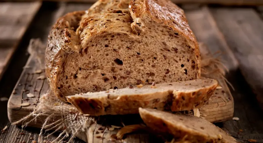 Frisch gebackenes Körnerbrot, angeschnitten auf einem Holzbrett. Perfekt, wann Brot aus der Form nehmen, um diese Kruste zu erhalten.