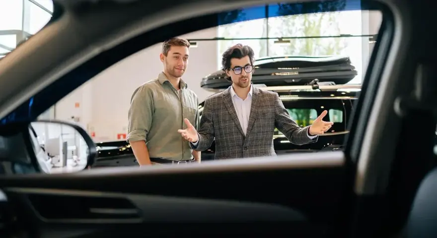 Dwóch mężczyzn w salonie samochodowym, jeden prezentuje auto.