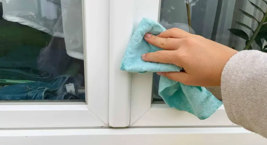 Hand reinigt mit blauem Tuch den weißen Rahmen eines Kunststofffensters.