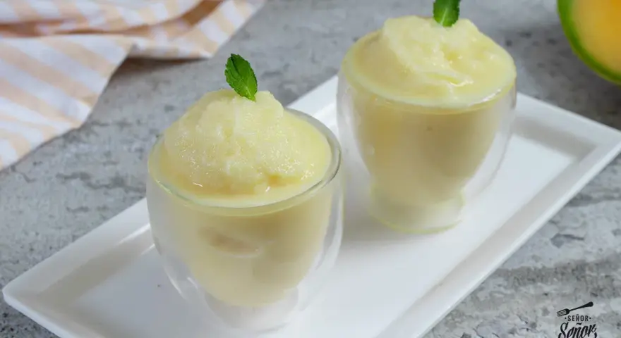 Dos copas de refrescante sorbete de melón, decoradas con hojas de menta, listas para disfrutar en un día caluroso.
