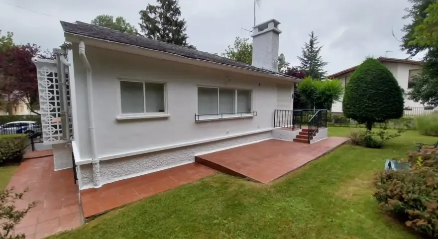 Terraza exterior con suelo de baldosas rojas recién pintado, rodeada de césped verde y un jardín frondoso.
