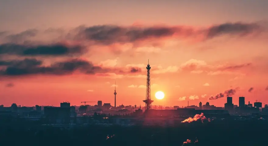Berlin bei Nacht von oben: Die Sonne geht unter und taucht den Himmel in ein feuriges Rot. Silhouetten von Türmen und Gebäuden zeichnen sich ab.