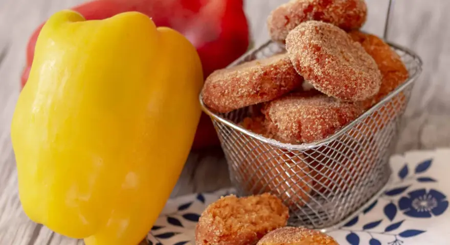 Polpette di peperoni dorate e croccanti, servite in un cestino, accanto a peperoni freschi rossi e gialli.