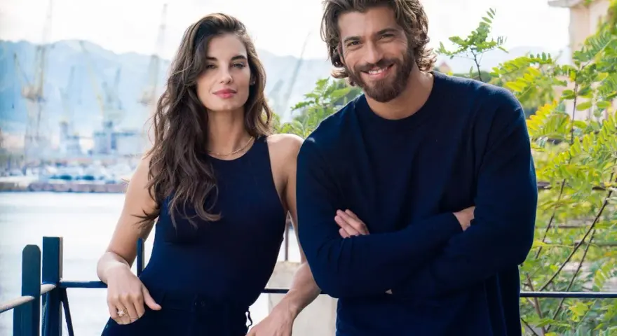 Coppia sorridente con sfondo di un porto, il suo sguardo è viola come il mare.