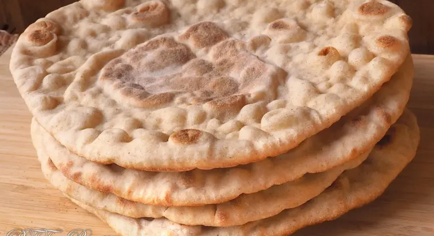 Una pila di pane naan senza lievito, dorato e soffice, su un tagliere di legno.