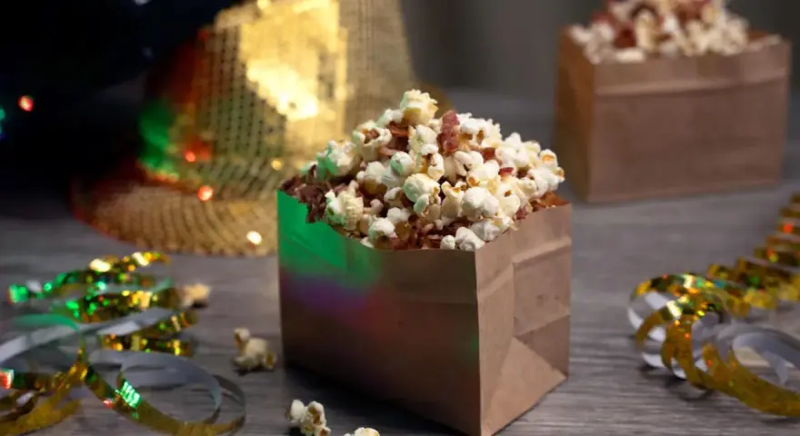 Festliga popcornboxar med bacon, redo för nyårsfirande. Glitterband och en paljetthatt i bakgrunden skapar en festlig stämning.
