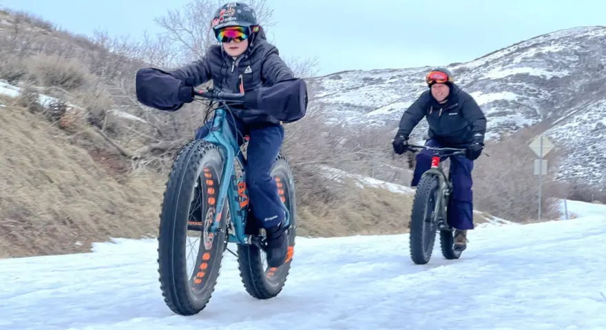 Two people ride fat tire bikes on a snowy path, demonstrating what are fat tire bikes for: tackling challenging winter terrain with their wide tires.