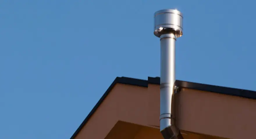 Scarico scaldabagno a gas in facciata, un tubo metallico lucido che sale verso il cielo azzurro, fissato al muro di un edificio.