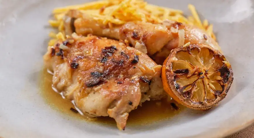 Delicioso pollo al limón con papas fritas crujientes y una rodaja de limón caramelizada.