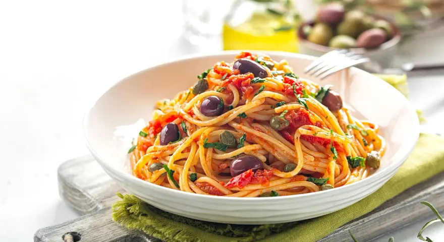 Un piatto invitante di spaghetti alla puttanesca, con olive nere, capperi e pomodoro, pronto per essere gustato.