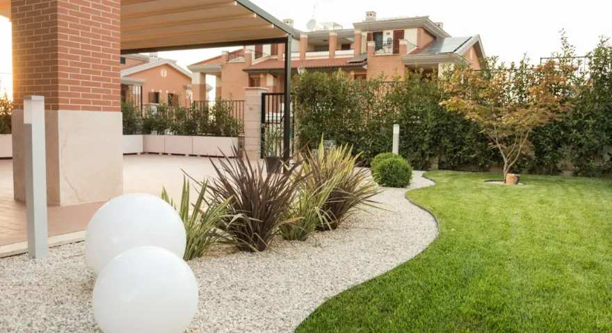 Giardino moderno con ghiaia bianca, sfere luminose e piante decorative. Belle idee giardino ingresso casa per un'accoglienza elegante.