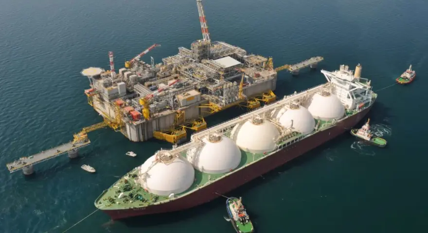 Praca na statku LNG: potężna jednostka z kopułami ładunkowymi przy platformie wydobywczej, holowniki asystują.
