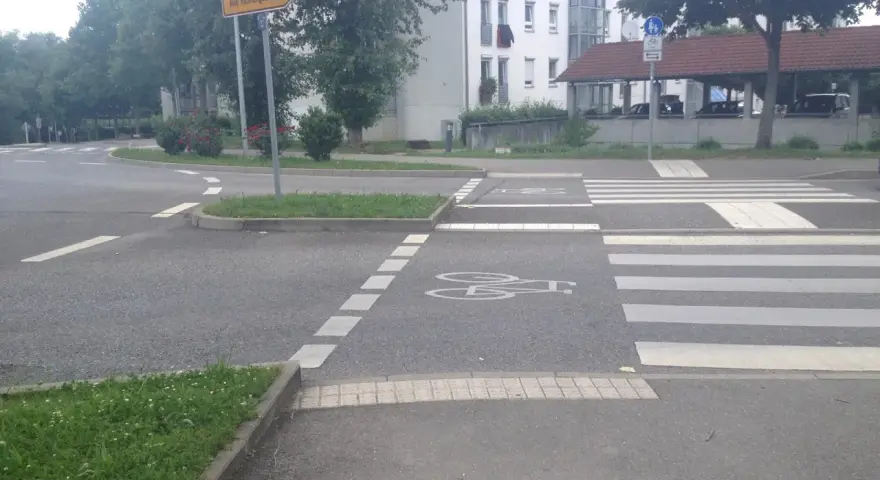 Ein Zebrastreifen mit Fahrradsymbolen auf dem Asphalt. Ein Schild weist in alle Richtungen.
