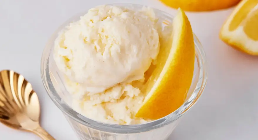 Erfrischendes Zitroneneis selber machen: Cremiges Eis im Glas mit Zitronenspalte und goldener Löffel.