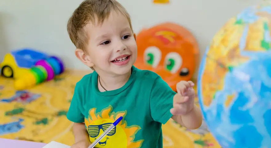 Uśmiechnięte polskie dziecko w hiszpańskiej szkole bawi się globusem i rysuje w zeszycie.