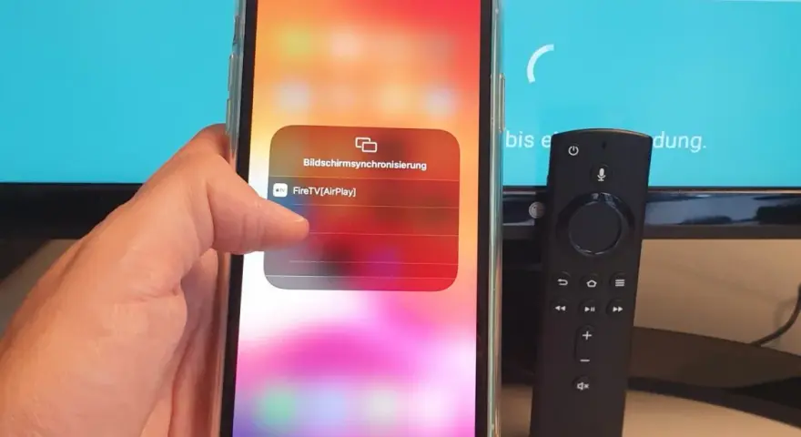 iPhone mit Fire TV Stick verbinden: AirPlay-Option wird auf dem iPhone angezeigt, daneben liegt die Fire TV Fernbedienung.