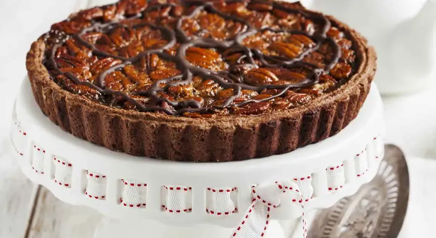 Deliziosa crostata al cioccolato con noci pecan caramellate e un elegante motivo di cioccolato fuso. Perfetta per ogni occasione.