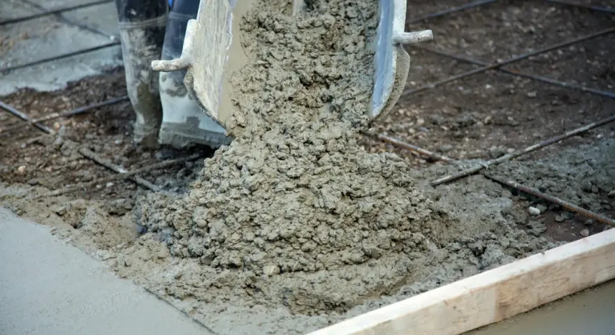 Wylewanie świeżego betonu na zbrojenie. Trwa naprawa betonu, widać buty pracownika i metalowe pręty.