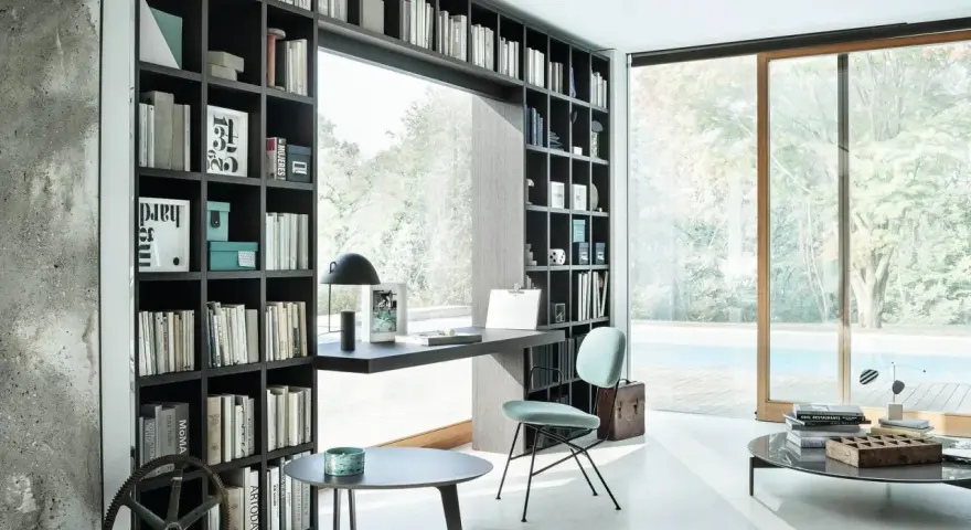 Libreria a muro con scrivania integrata, perfetta per idee stanza studio piccola. Sedia azzurra, tavolini neri e vista piscina.