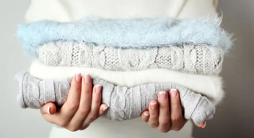 Pile de pulls en laine douce, gris et blanc, avec un pull bleu ciel. Idéal pour savoir comment detacher un pull blanc et le garder comme neuf.
