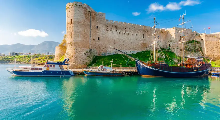 Zamek Kyrenia na Cyprze Północnym z łodziami przycumowanymi w turkusowej zatoce.