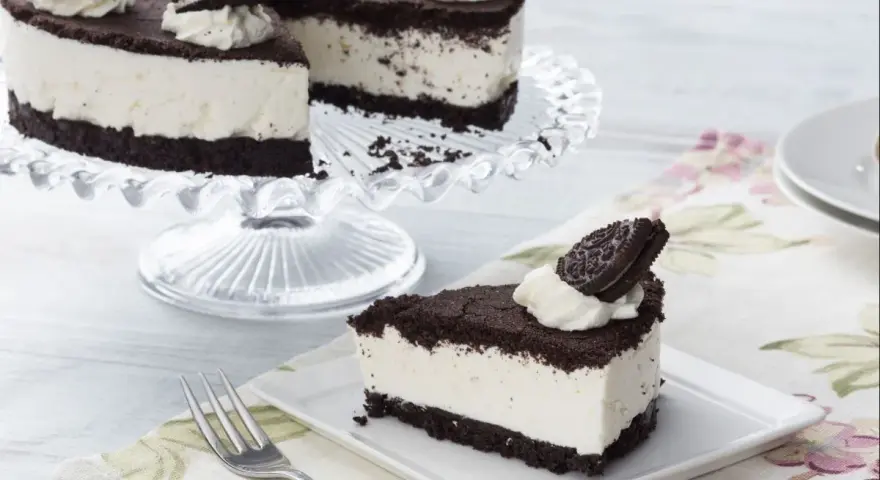 Una deliciosa tarta de oreo, con una base de galleta oscura y un cremoso relleno blanco, decorada con nata y galletas oreo.